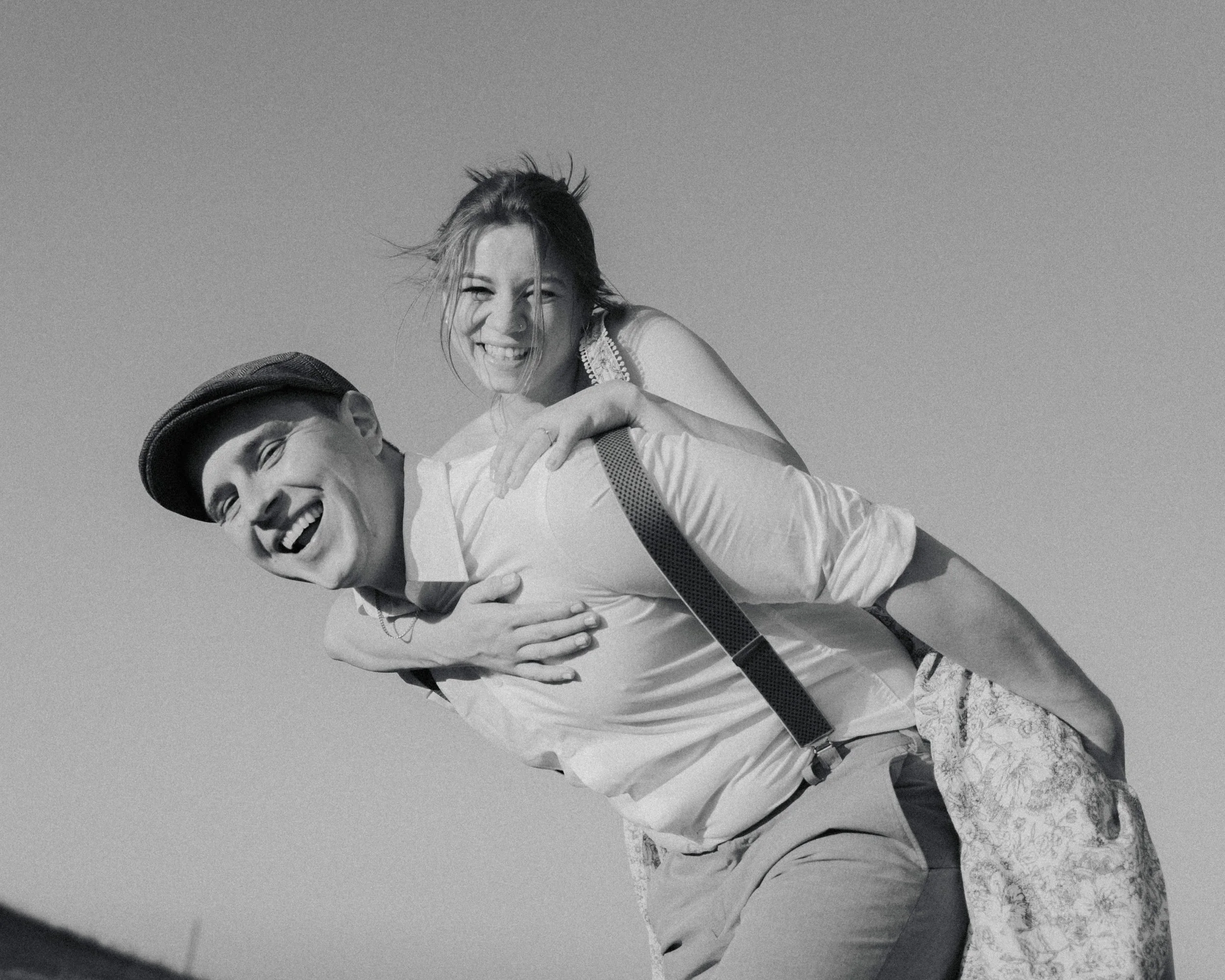 Brautpaar, Braut sitzt Huckepack auf ihrem Bräutigam, beide lachen und fragen sich was ein Hochzeitsfotograf im Zürcher Oberland wohl kostet.
