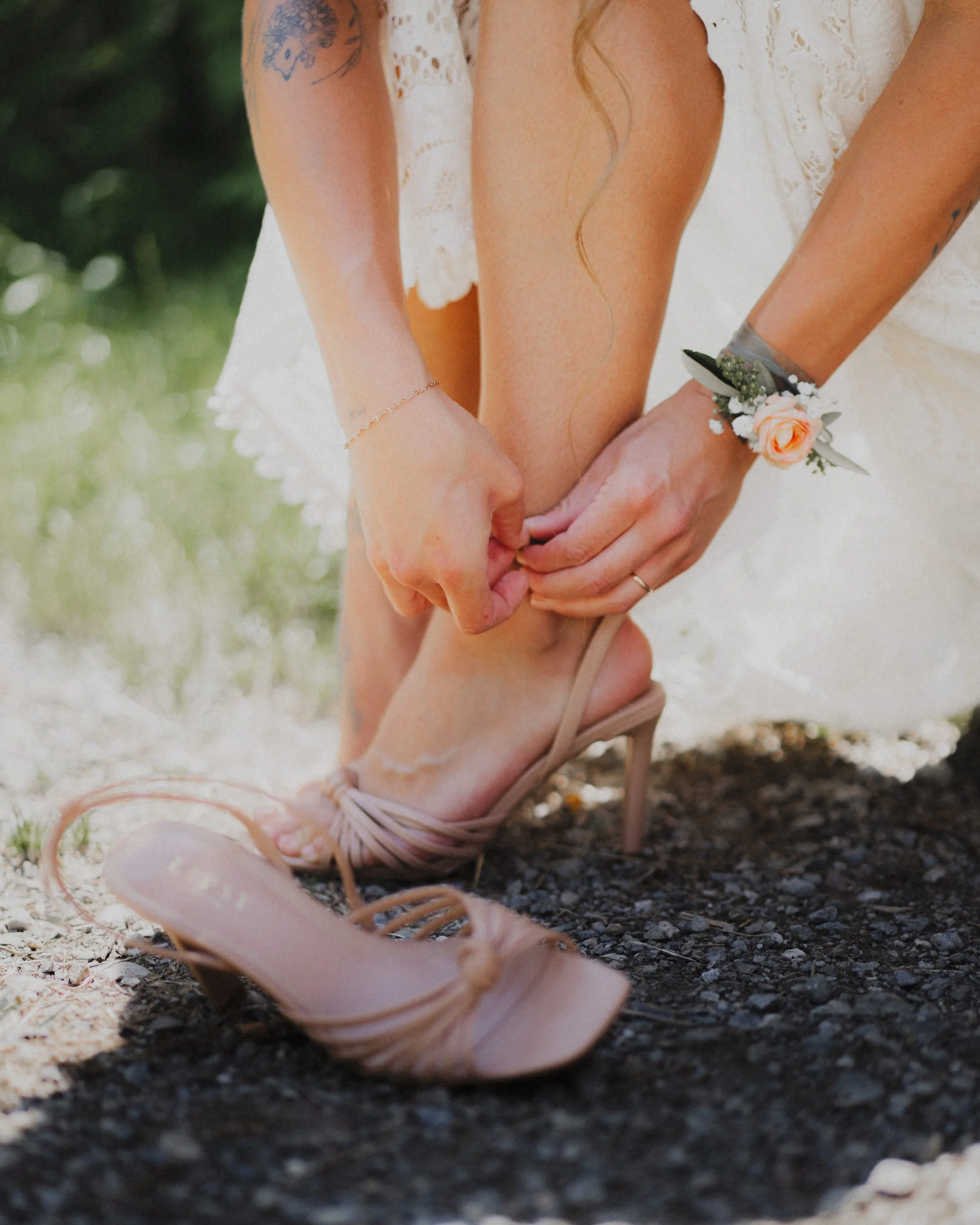 Nahaufnahme von einem Brautpaar, das einen Händedruck macht. Das Paar trägt Brautkleider und Schuhe, die auf einem Boden aus Erde liegen. Das Brautpaar zeigt eine liebevolle Geste bei ihrer Hochzeit.