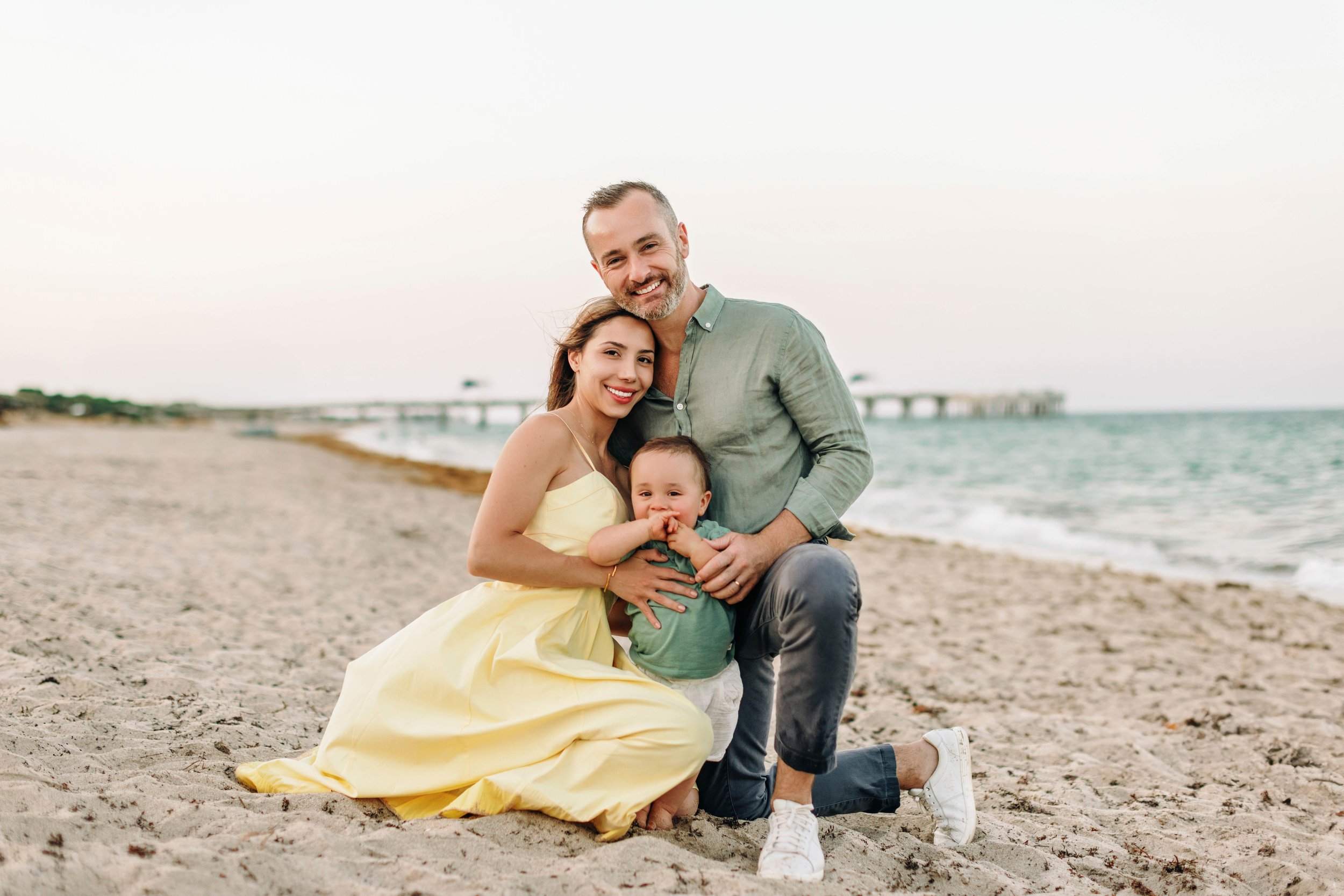Parents and baby smiling together during a beach family session in Pompano Beach.