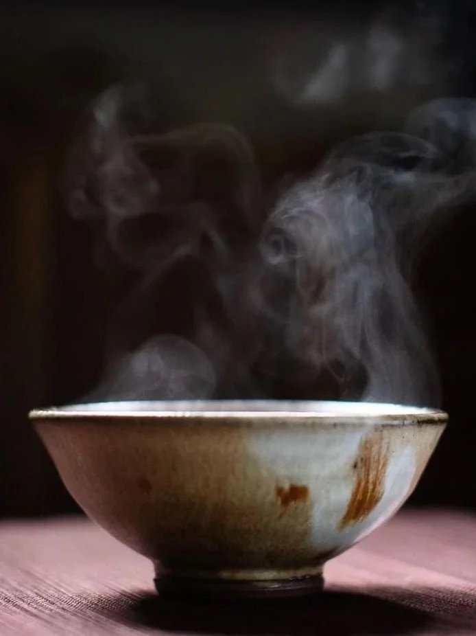 Steaming bowl of hot food or beverage on a wooden surface with dark background
