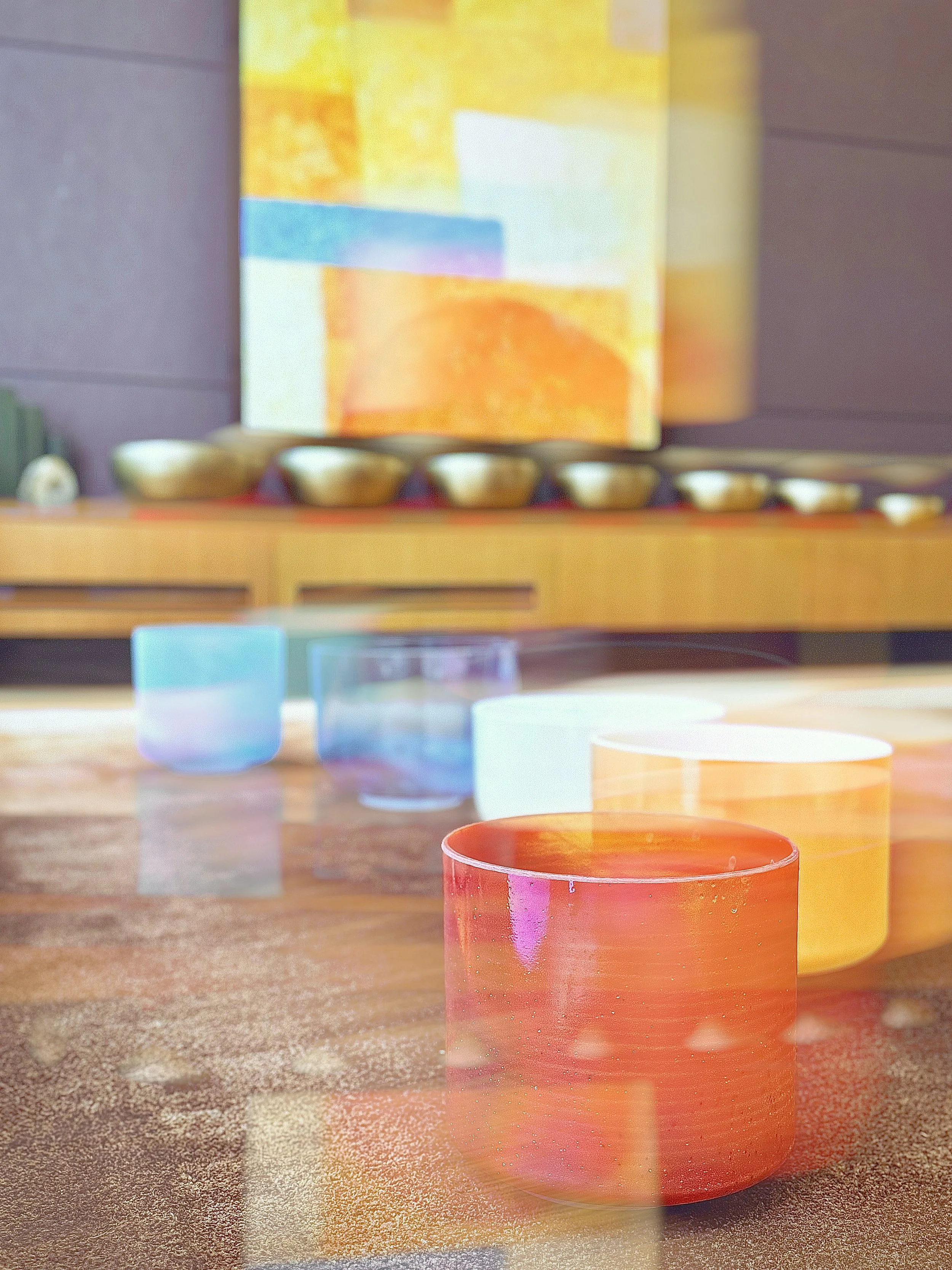 Colorful stained glass cups on a wooden table with colorful abstract artwork in the background.