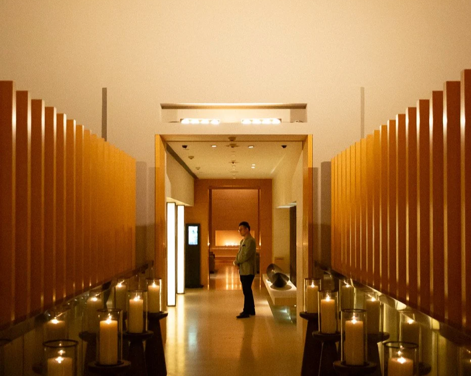 A man standing in a dimly lit hallway with candles on both sides, wooden wall panels, and a modern design.