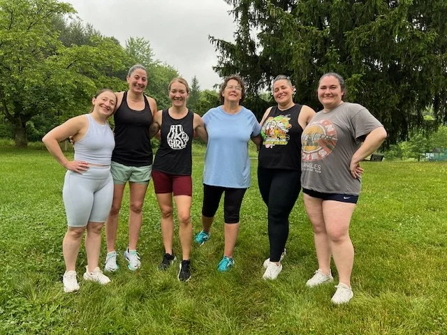 Women of all ages posing outside on the grass after strength training with Mostly Well at our Summer Camp wellness event