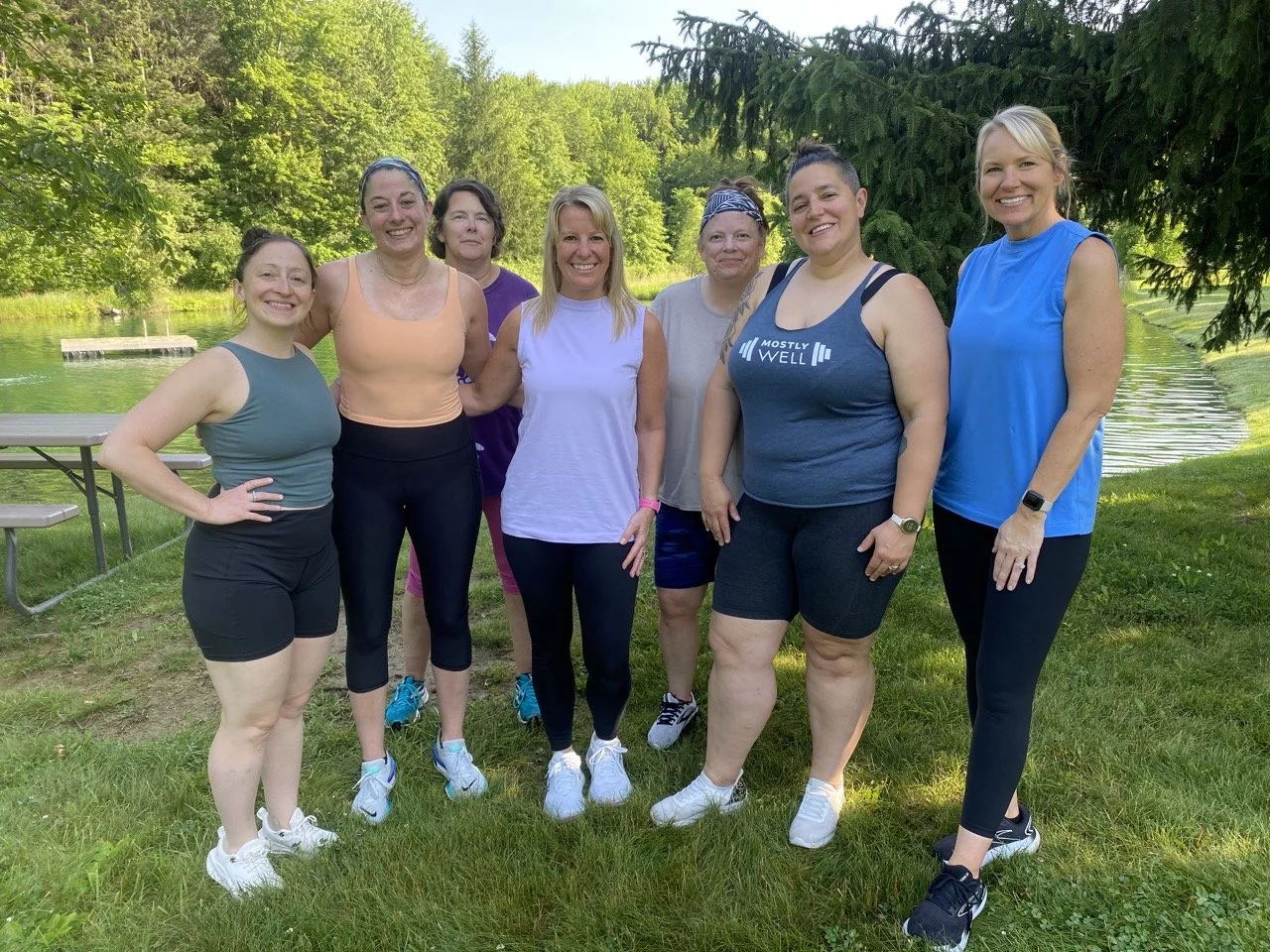 Strong women posing outside in their workout clothes at Mostly Well's Summer Camp wellness event