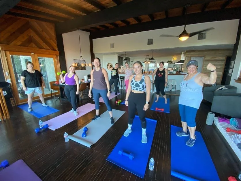 Women of all ages posing for a photo on their yoga mats after strength training with Mostly Well at a wellness event