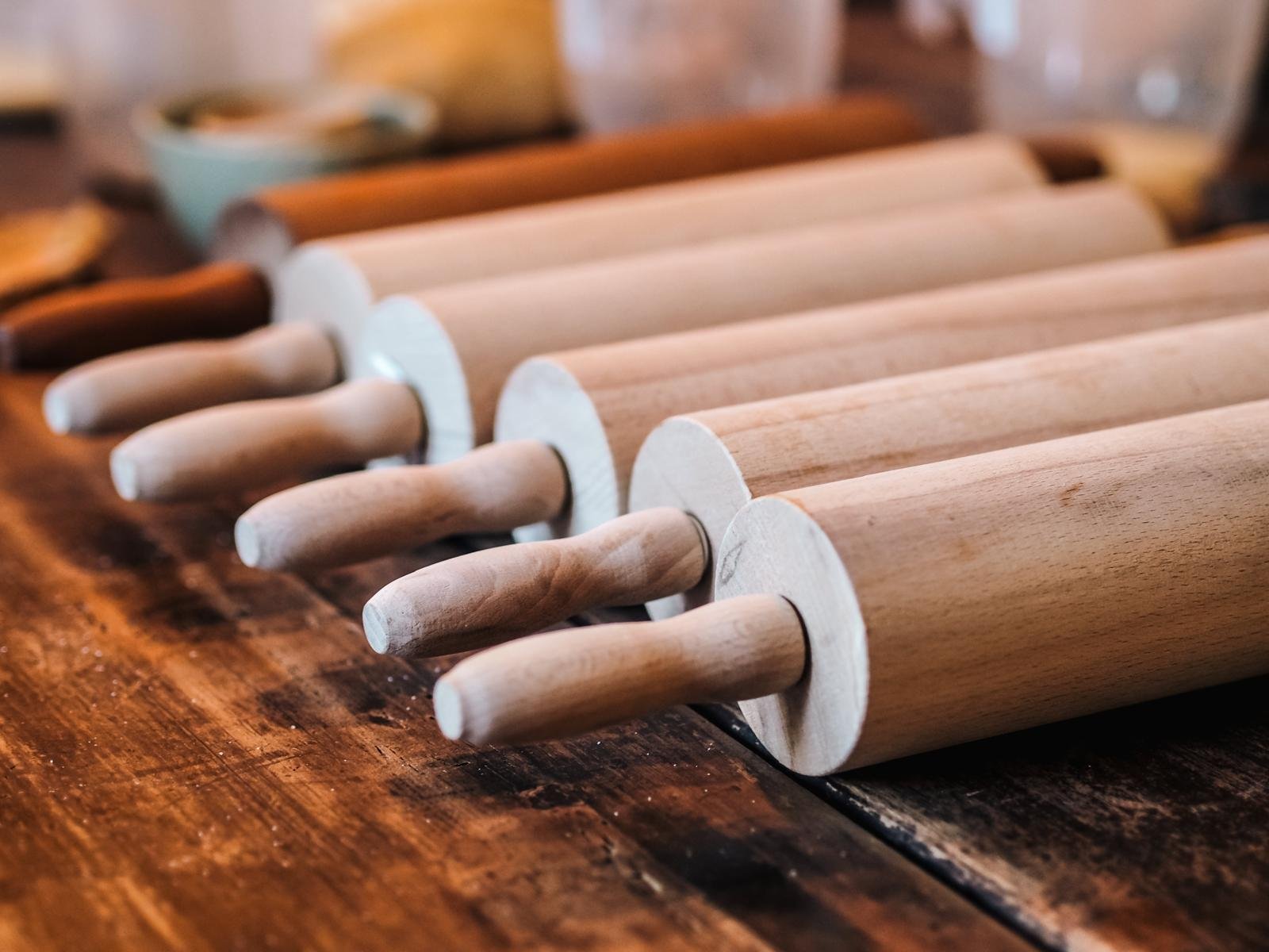 Multiple wooden rolling pins arranged in a row on a wooden surface.