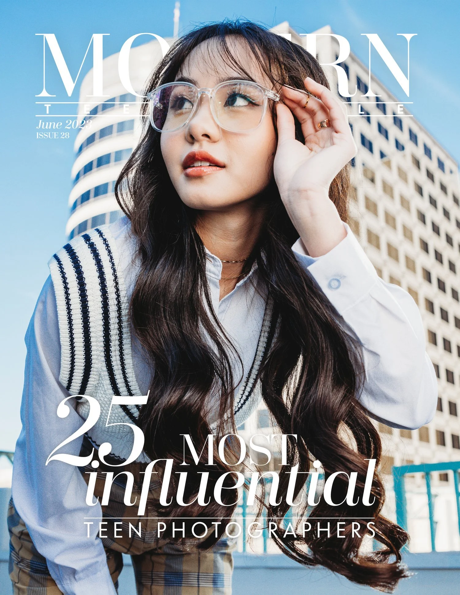 Teen girl with long dark hair, glasses, and a white shirt posing outdoors with a city skyscraper behind her. Magazine cover with text about influential teen photographers.