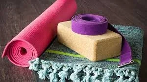 Yoga mat, foam blocks, and a purple strap on a wooden floor.
