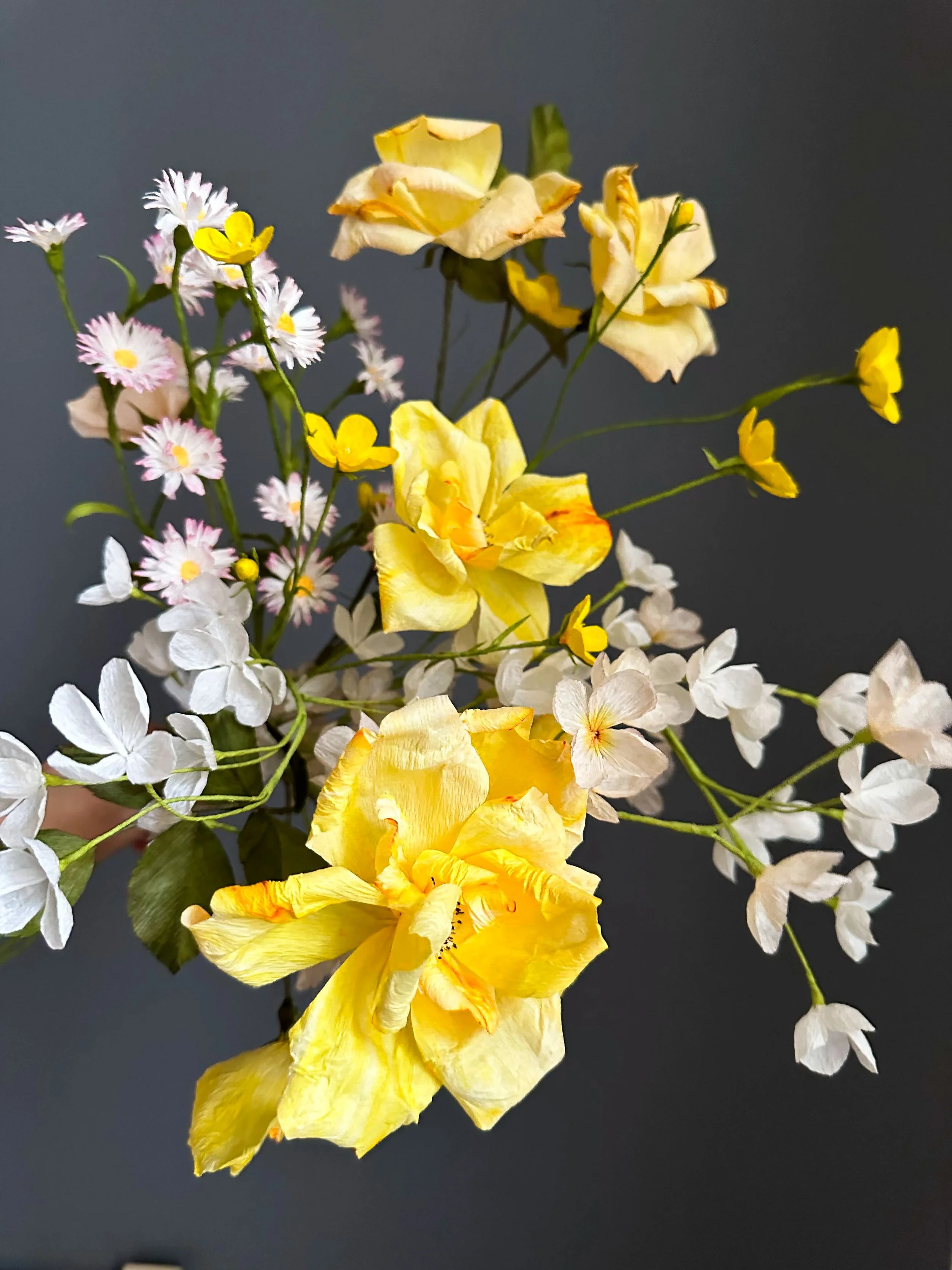 En farverig buket af gule, hvide, og lyserøde blomster mod en mørk baggrund.