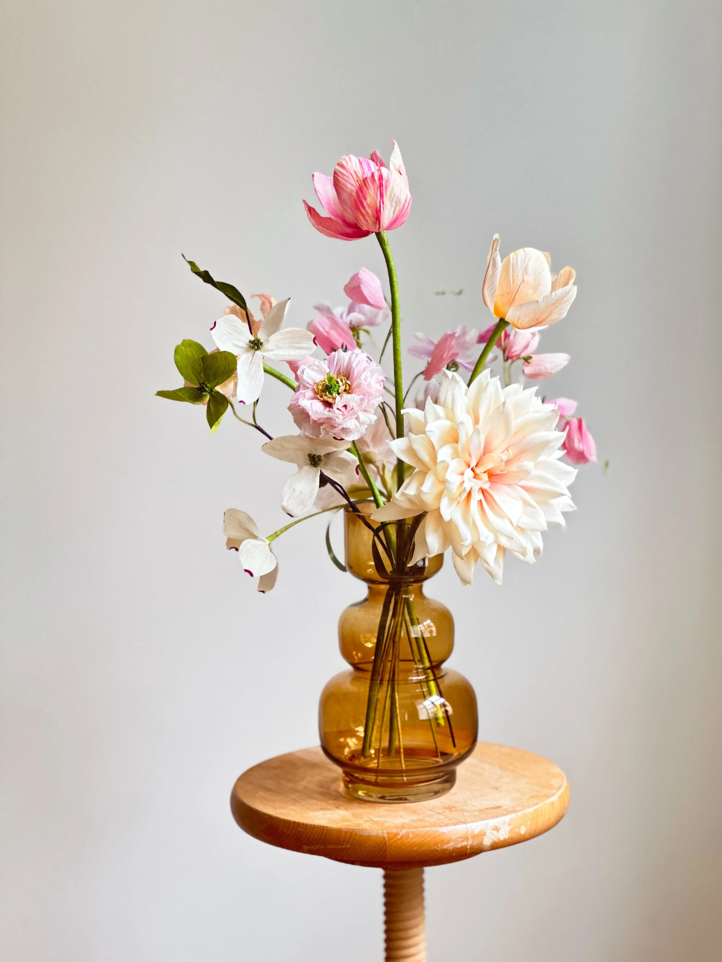 En række blomster i en amberfarvet vase på en rund træstol.