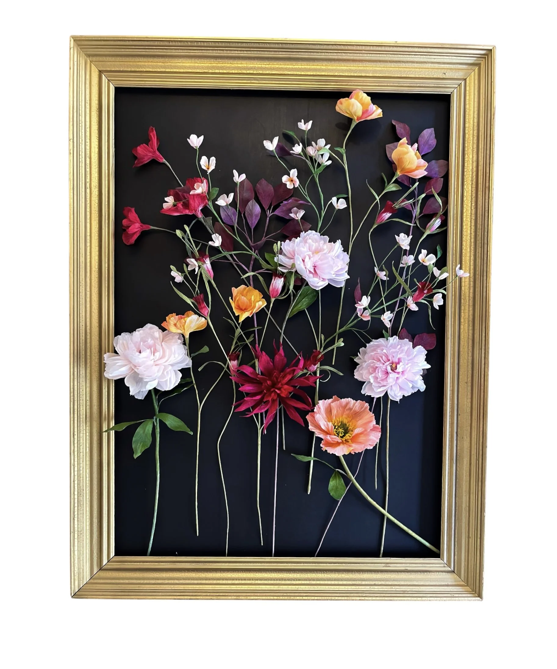 Blomster lavet af papirsbånd i en guldramme, sat op på sort baggrund.