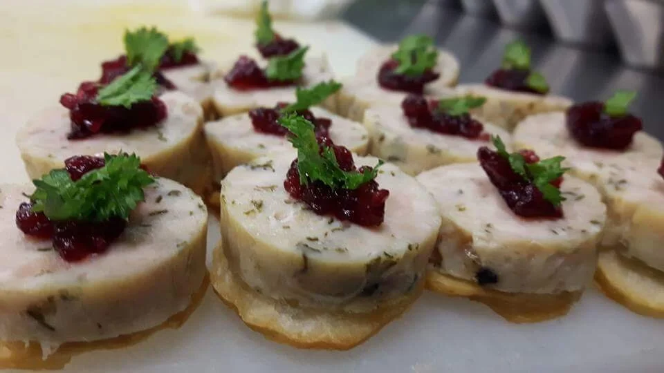 Close Up image of crackers topped with medallions of herbed cheese, small dollops of red jam, and each adorned with fresh green herb.