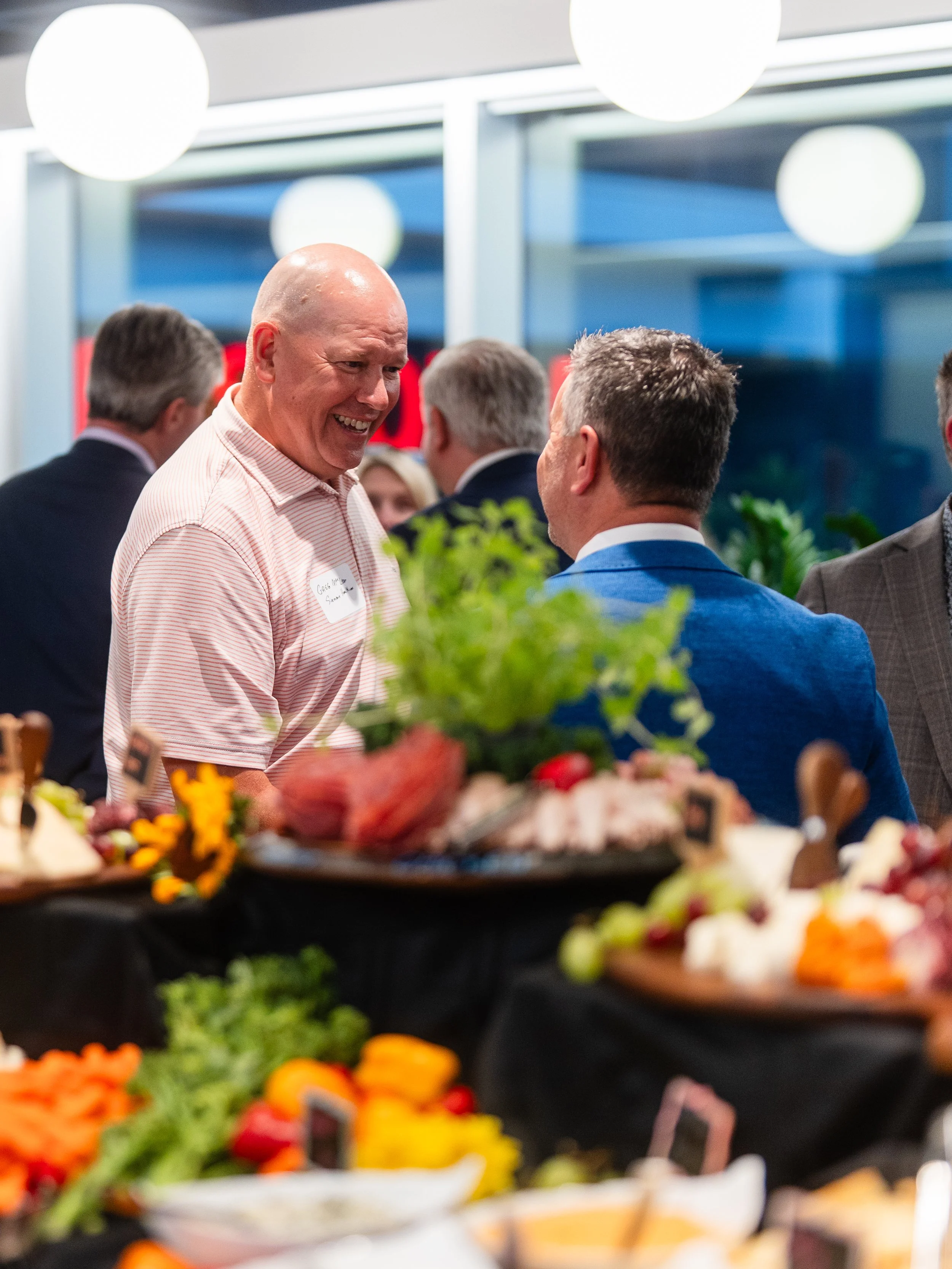 Two men with light toned skin smile and converse behind a colorful grazing table