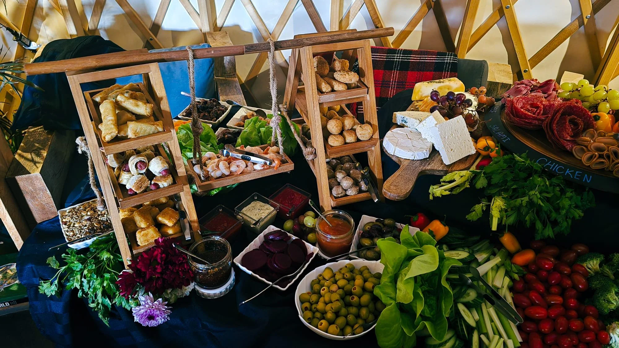 Multi-tiered grazing table with small pastries, charcuterie, cheese, crackers, vegetables, olives and spreads