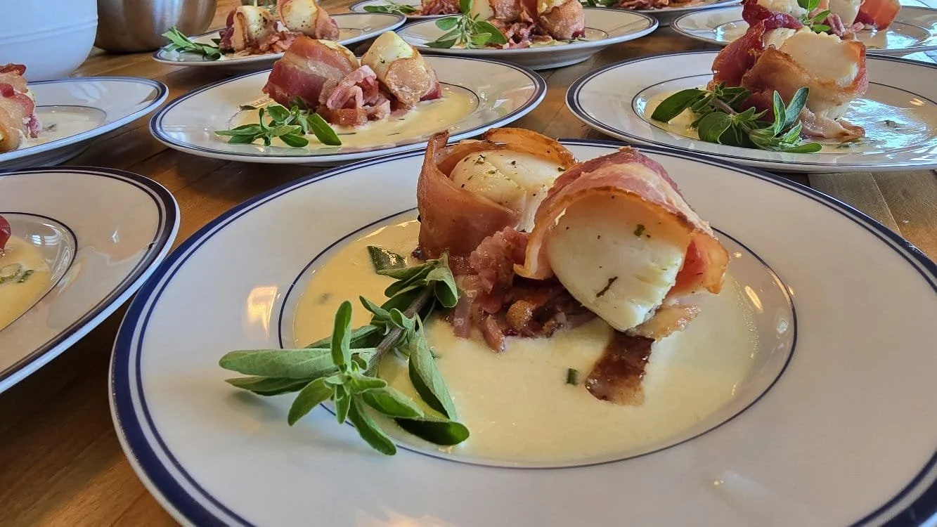 Close up photo of bacon-wrapped scallops with cream sauce and herbs