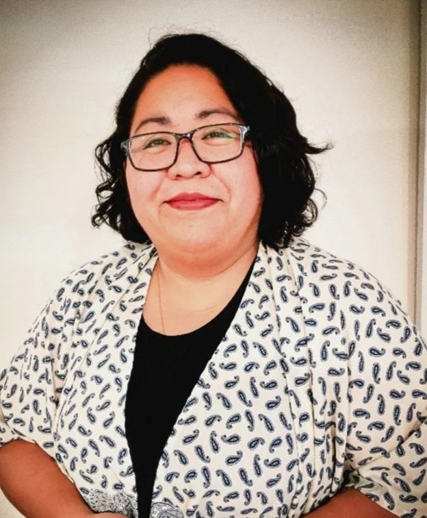 A woman with dark wavy hair and glasses wears a white and black jacket