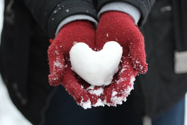 A heart made of snow lies in gloved hands