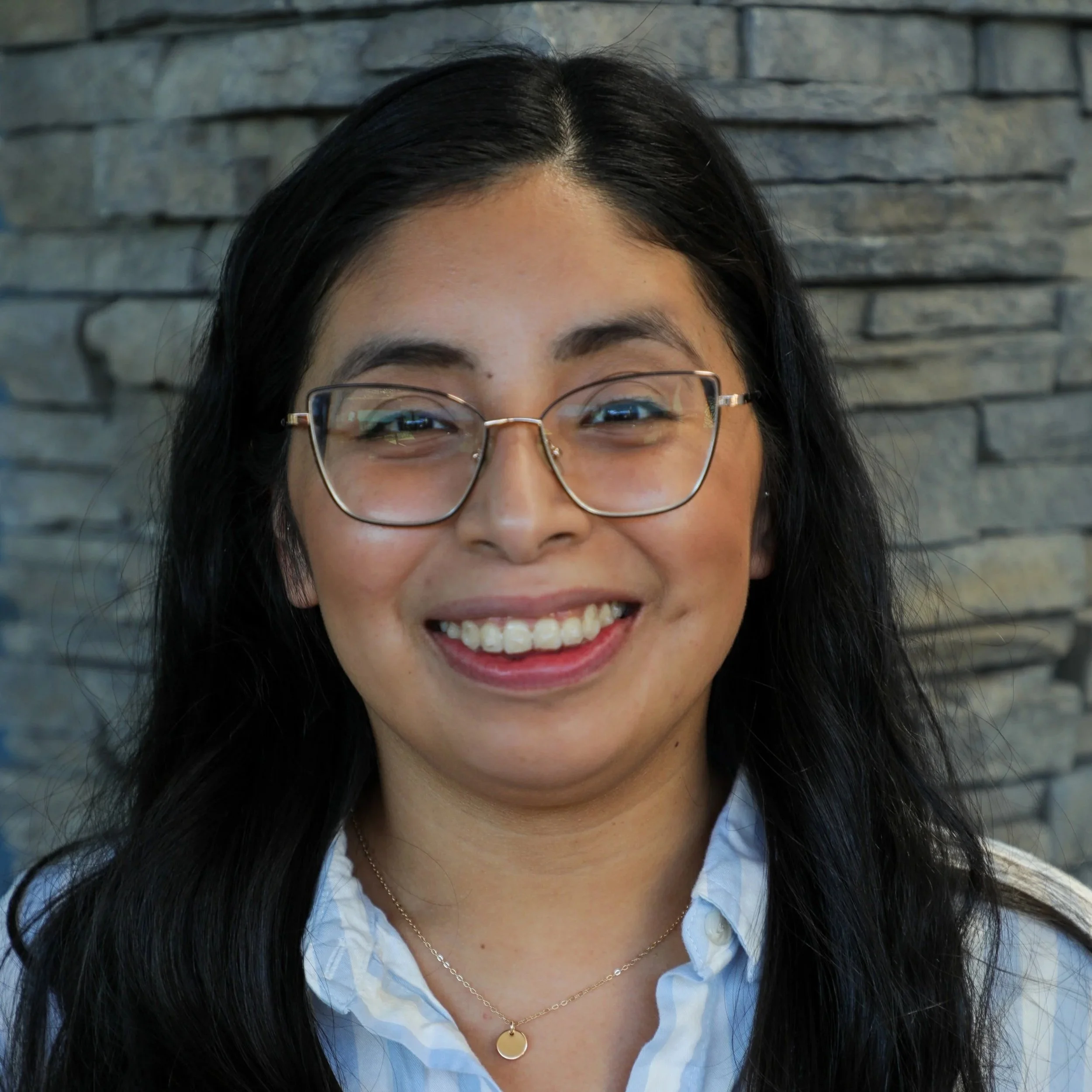 Britania is shown with dark eyes behind glasses and long black hair and wearing a blue and white striped shirt