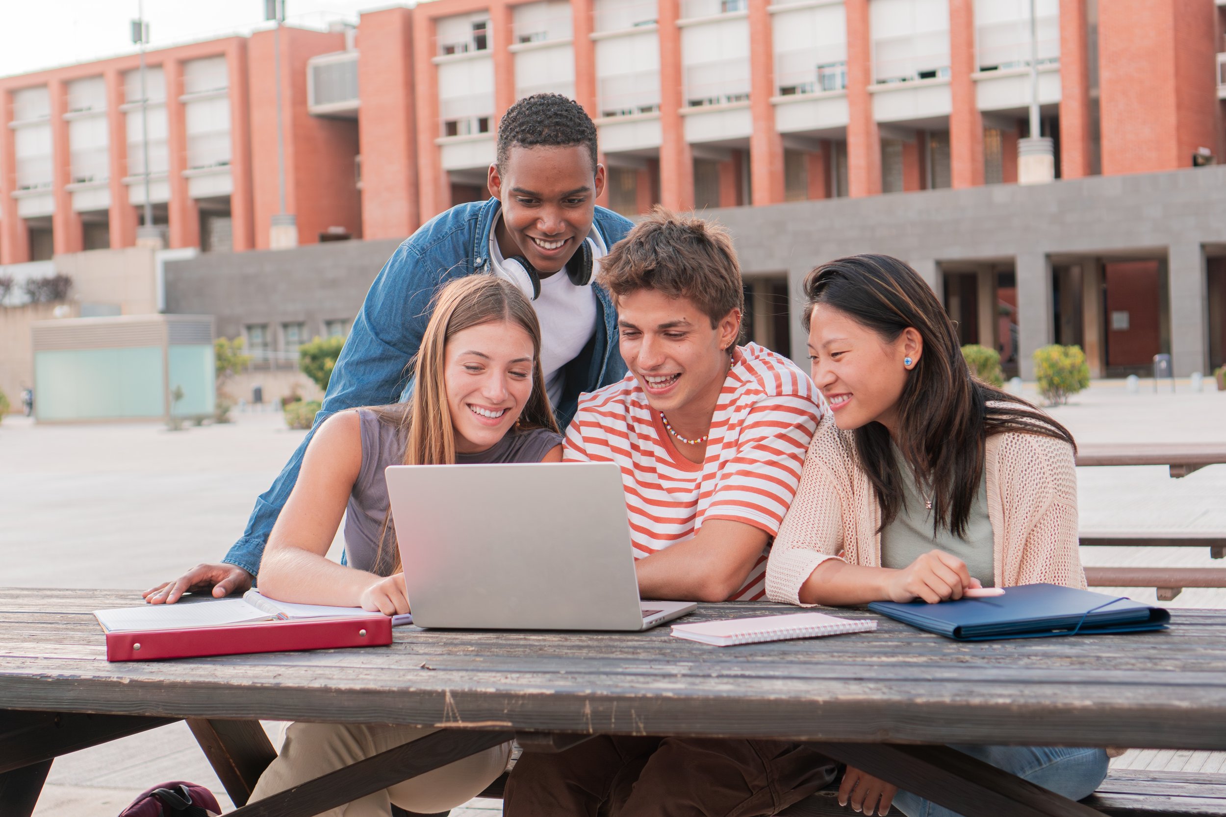 High school students and a teacher meet at a picnic table outside a high school building