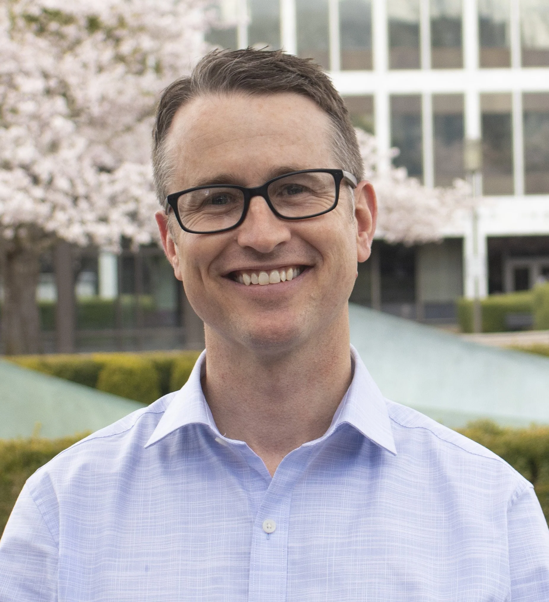 man in light blue collared shirt in front of blooming cherry trees