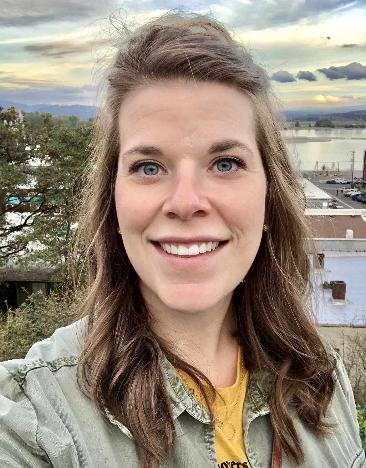 a smiling woman with brown hair and a waterfront cityscape behind her
