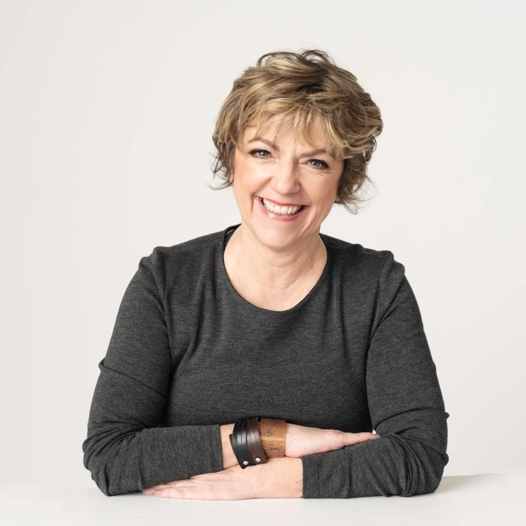 Woman with sandy short hair crosses her arms and smiles in front of a white background