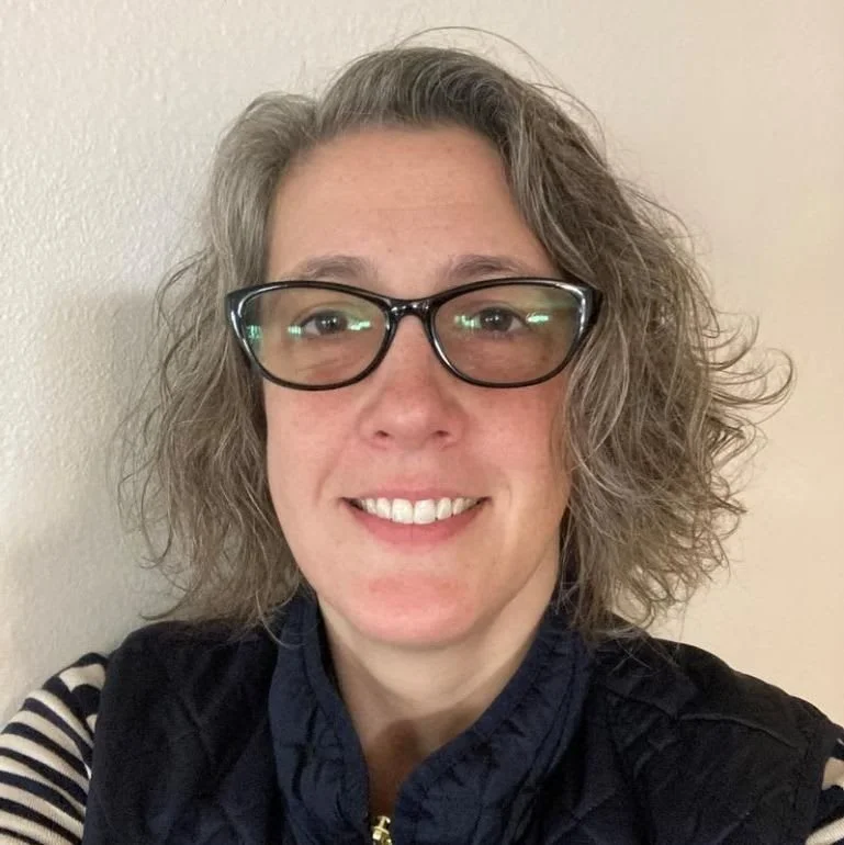 Person with glasses smiles in a black top