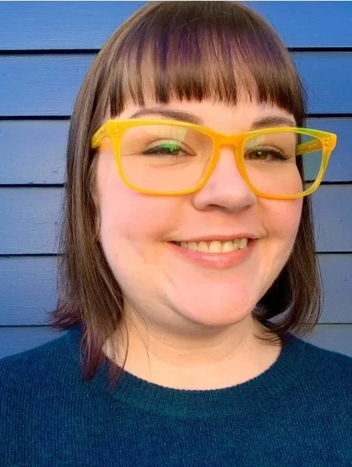 woman with fun yellow glasses and brown hair smiles
