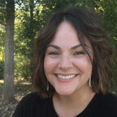A woman with short wavy brown hair and dark eyes smiles