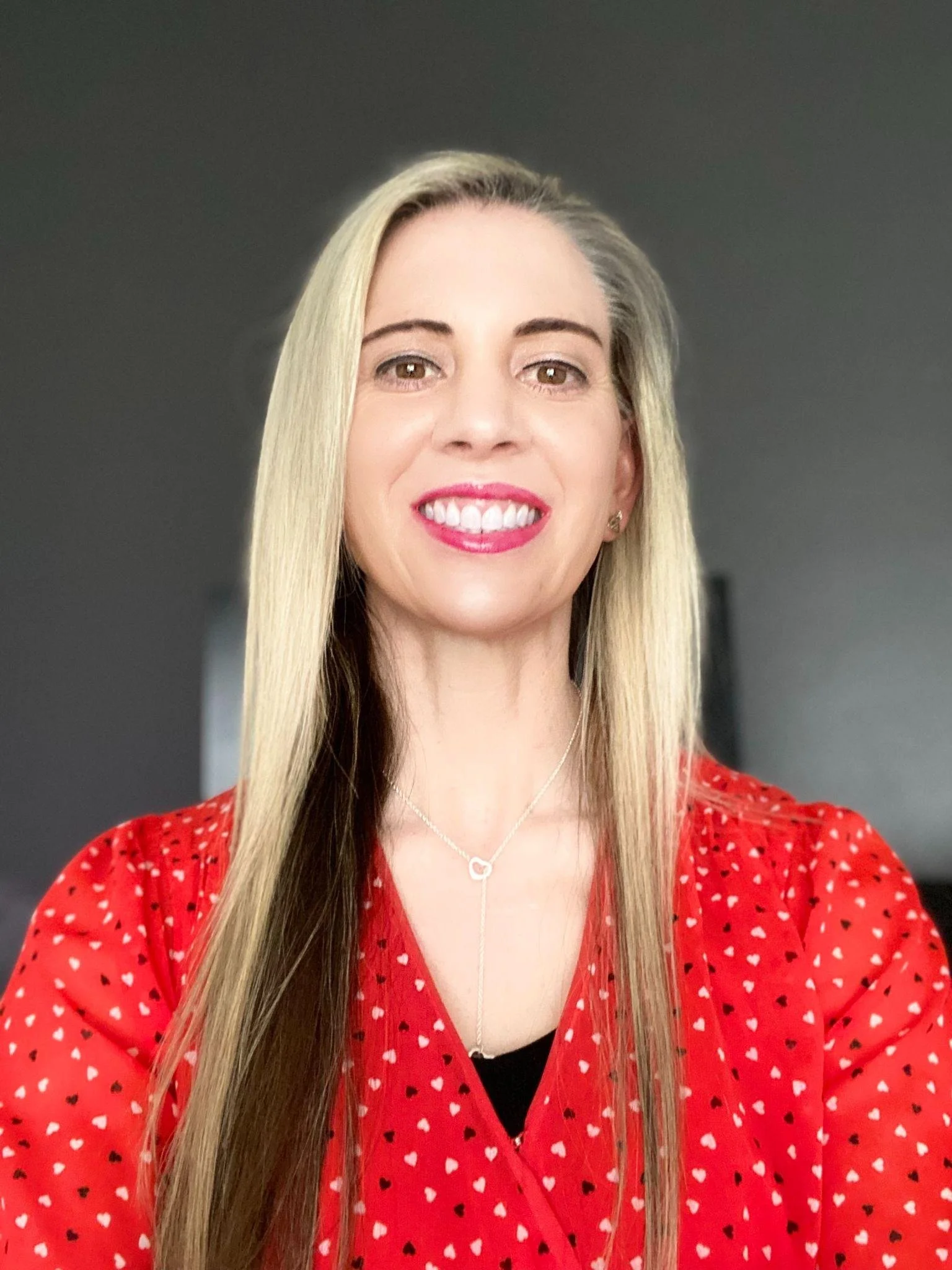 A woman with long blond hair wears a red polka-dot blouse.