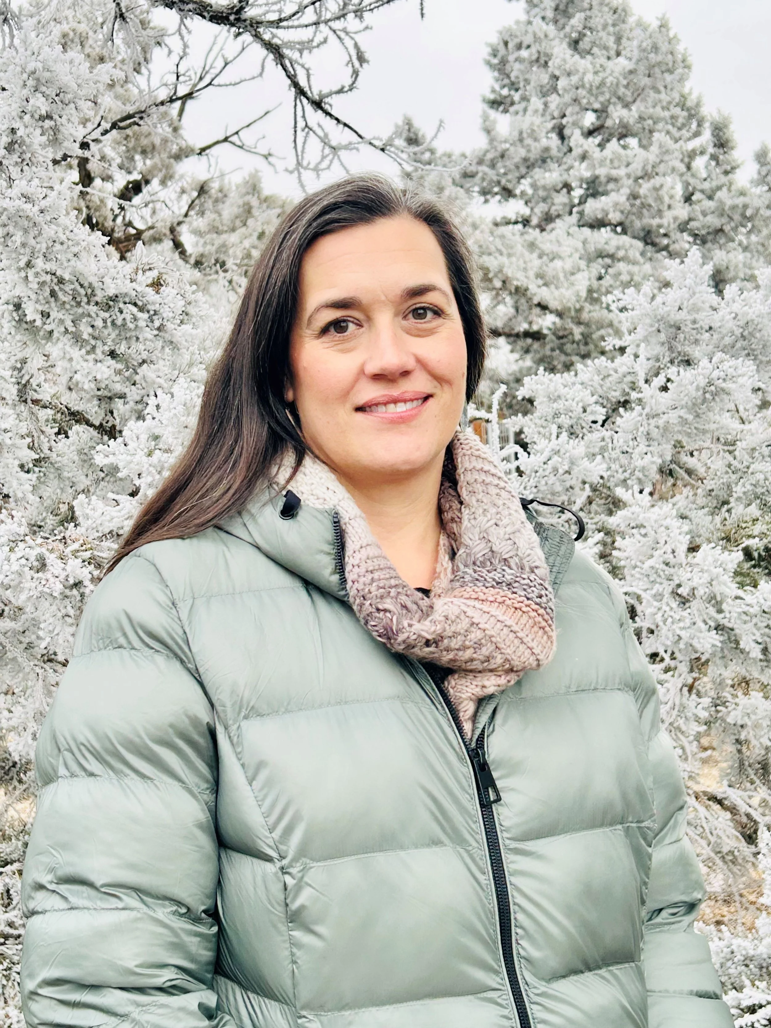 Woman with long brown hair smiling in front of a winter landscape