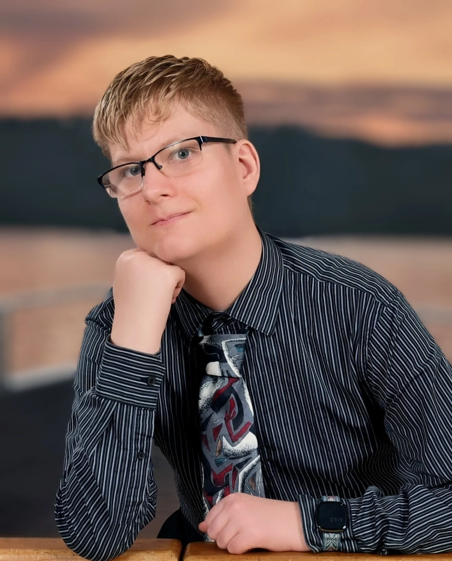 Young man with blonde hair styled to the front wears glasses and a button-down striped shirt and tie