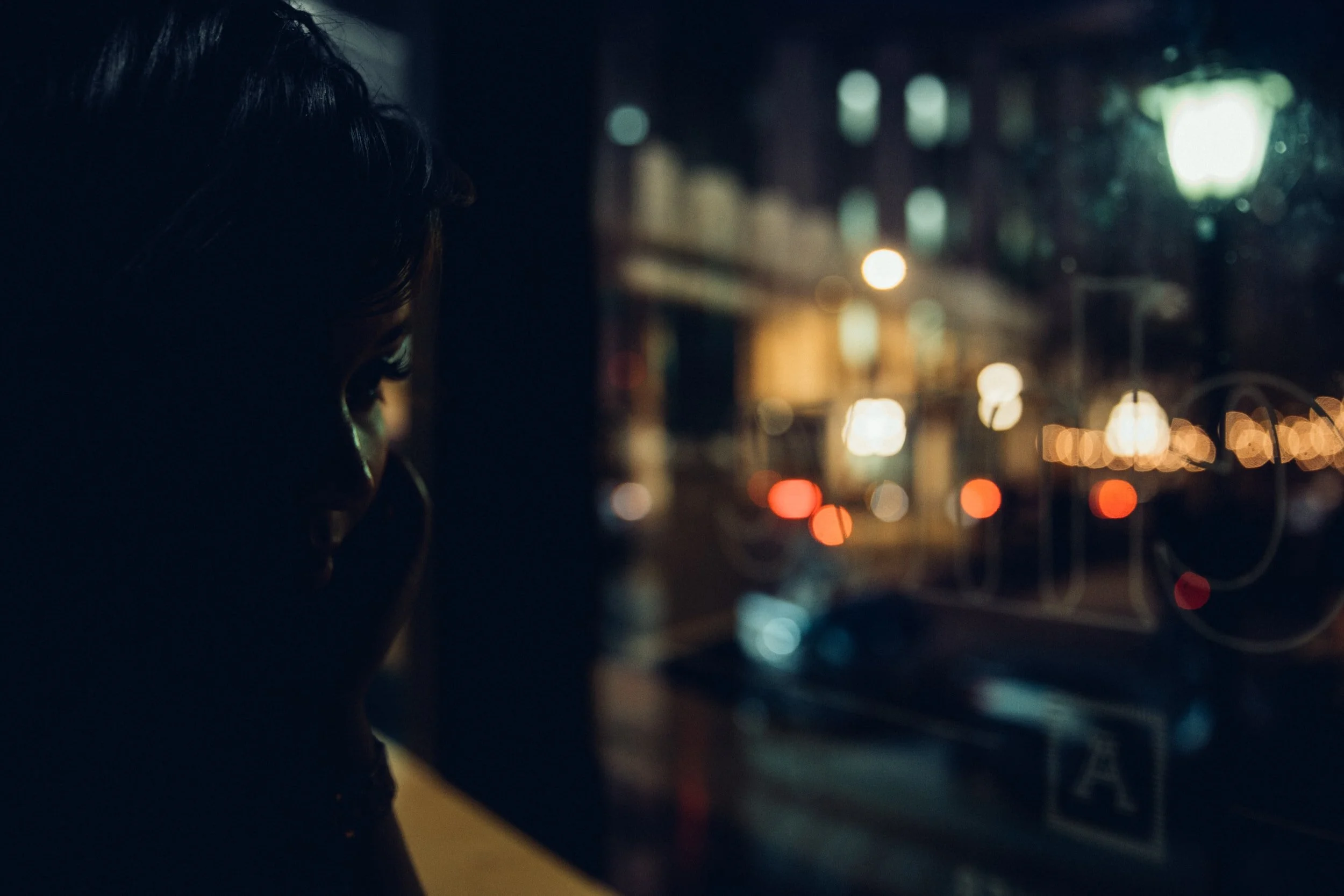 Silhouette of a person looking out a window at a cityscape with blurred lights at night.