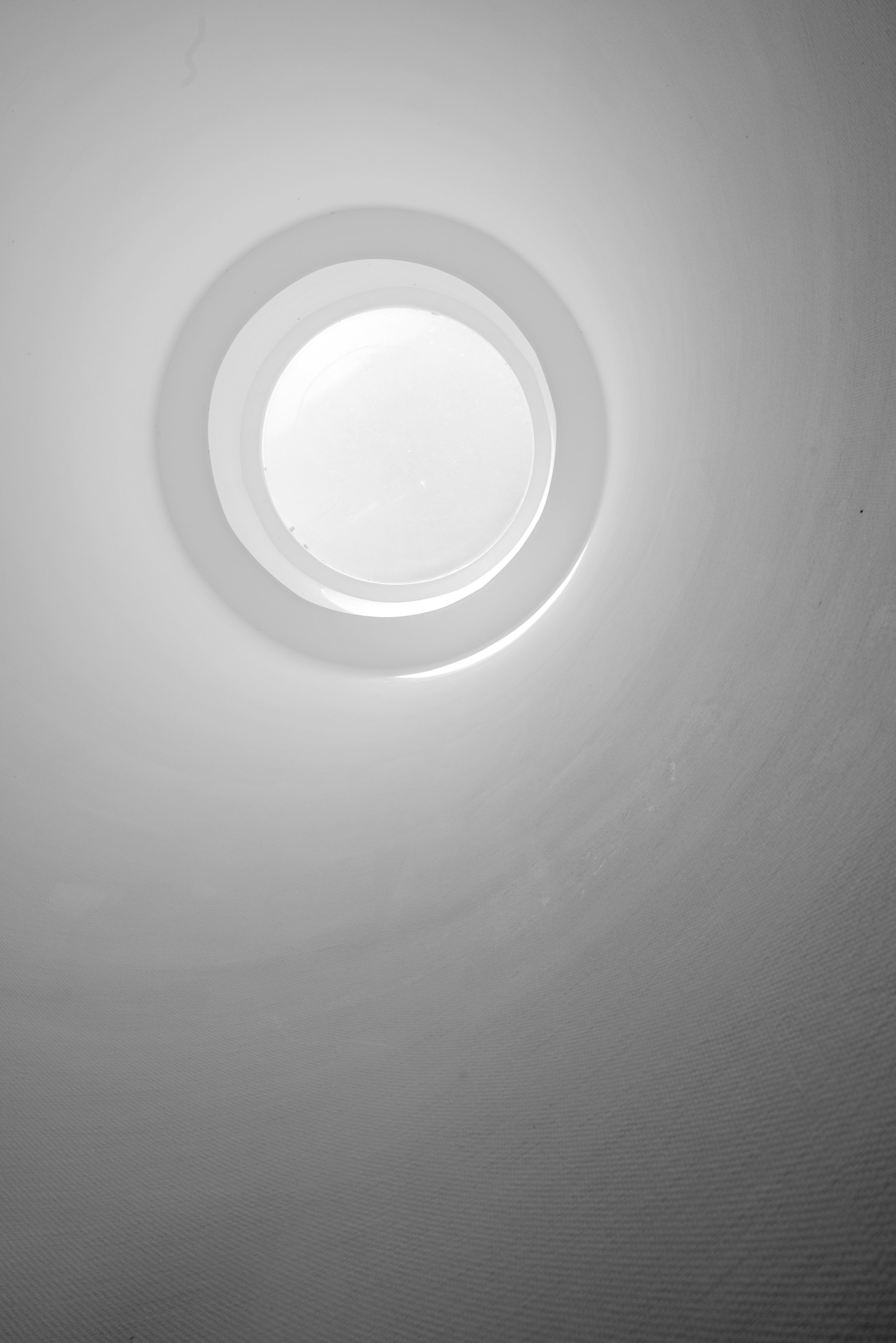 Close-up van een ronde lichtbron, mogelijk een plafondlamp, met een witte, gladde omlijsting en witte muur eromheen.