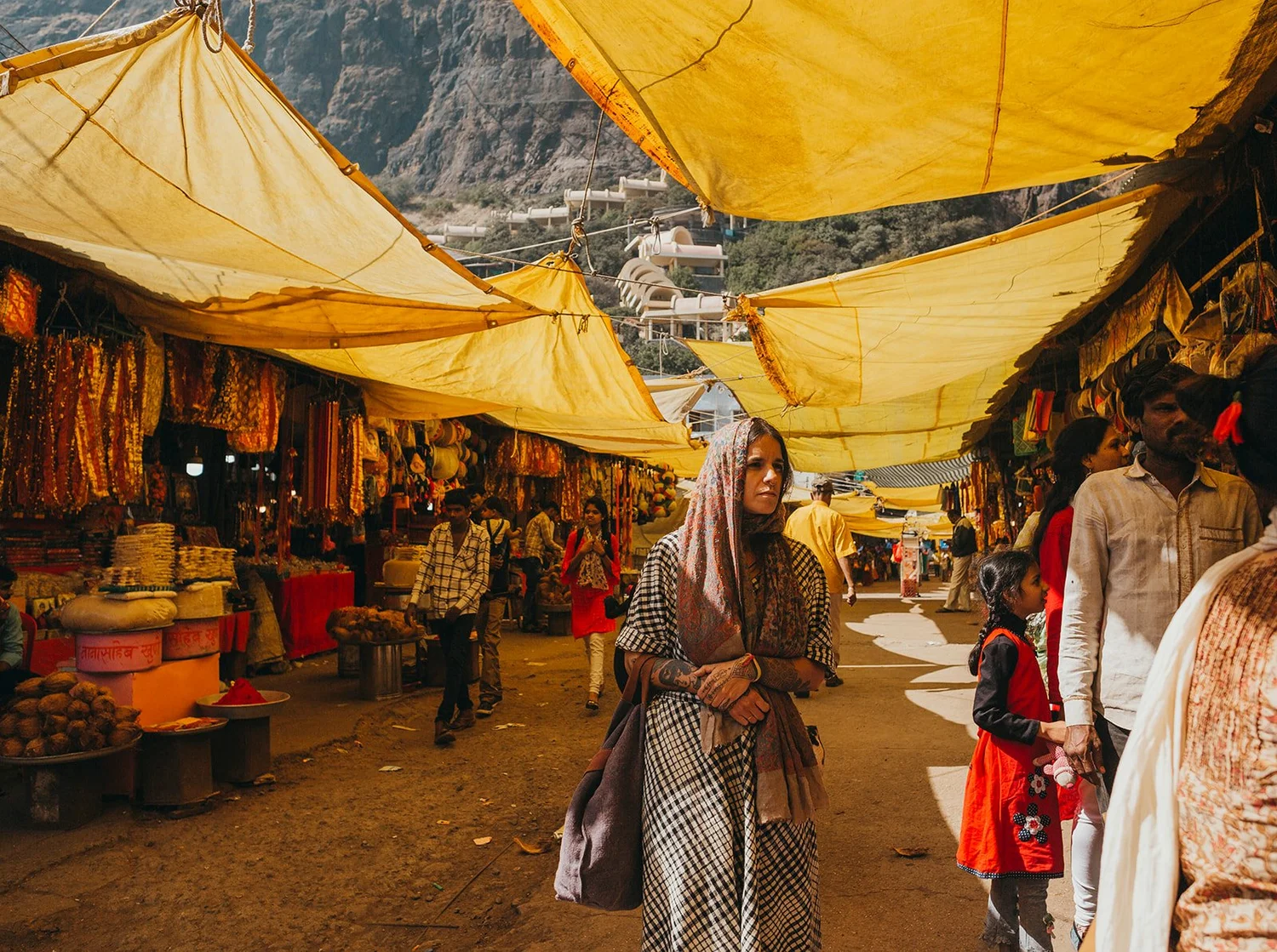 A woman in a shawl walking through a temple bazaar under yellow canopies