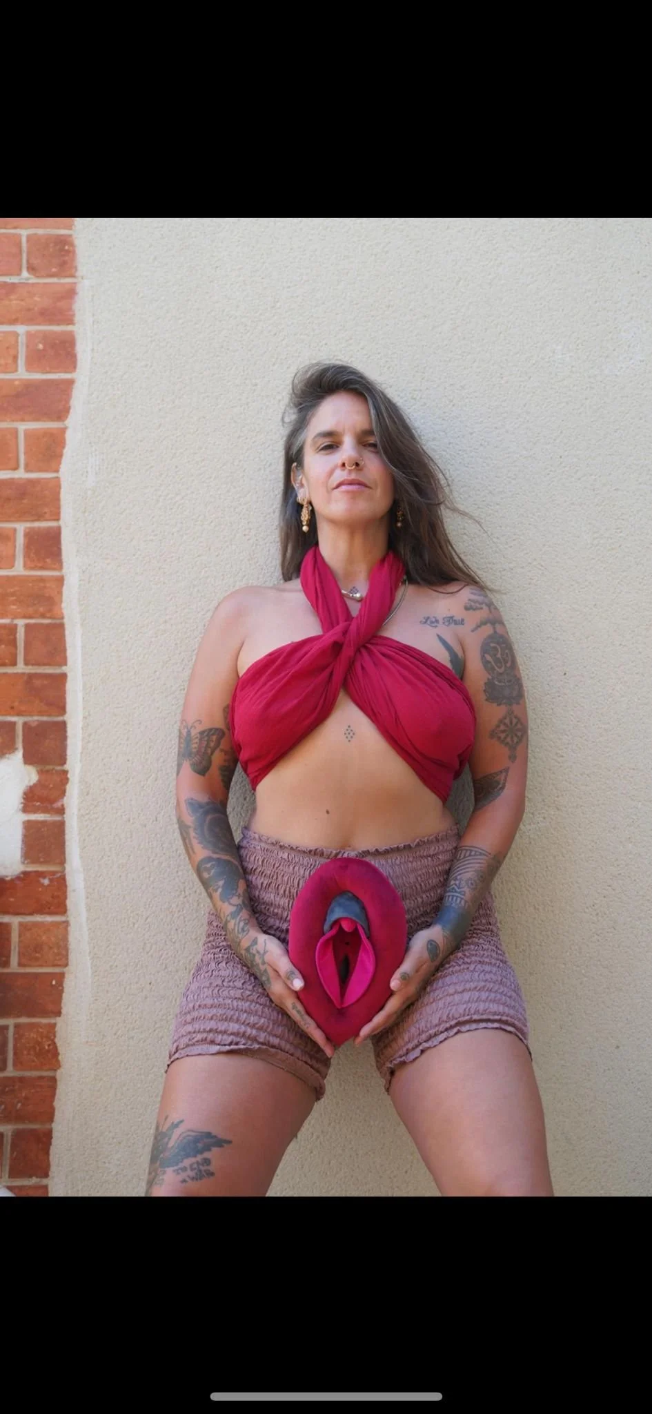 Adriana Rizzolo standing against a beige wall, holding a tied red cloth in front of her body