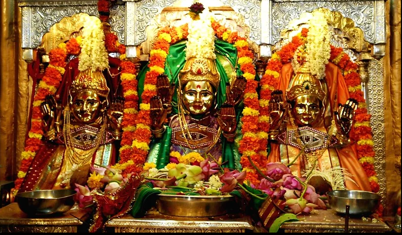 Hindu deities decorated with flowers, jewelry, and colorful garments, placed on an ornate altar.