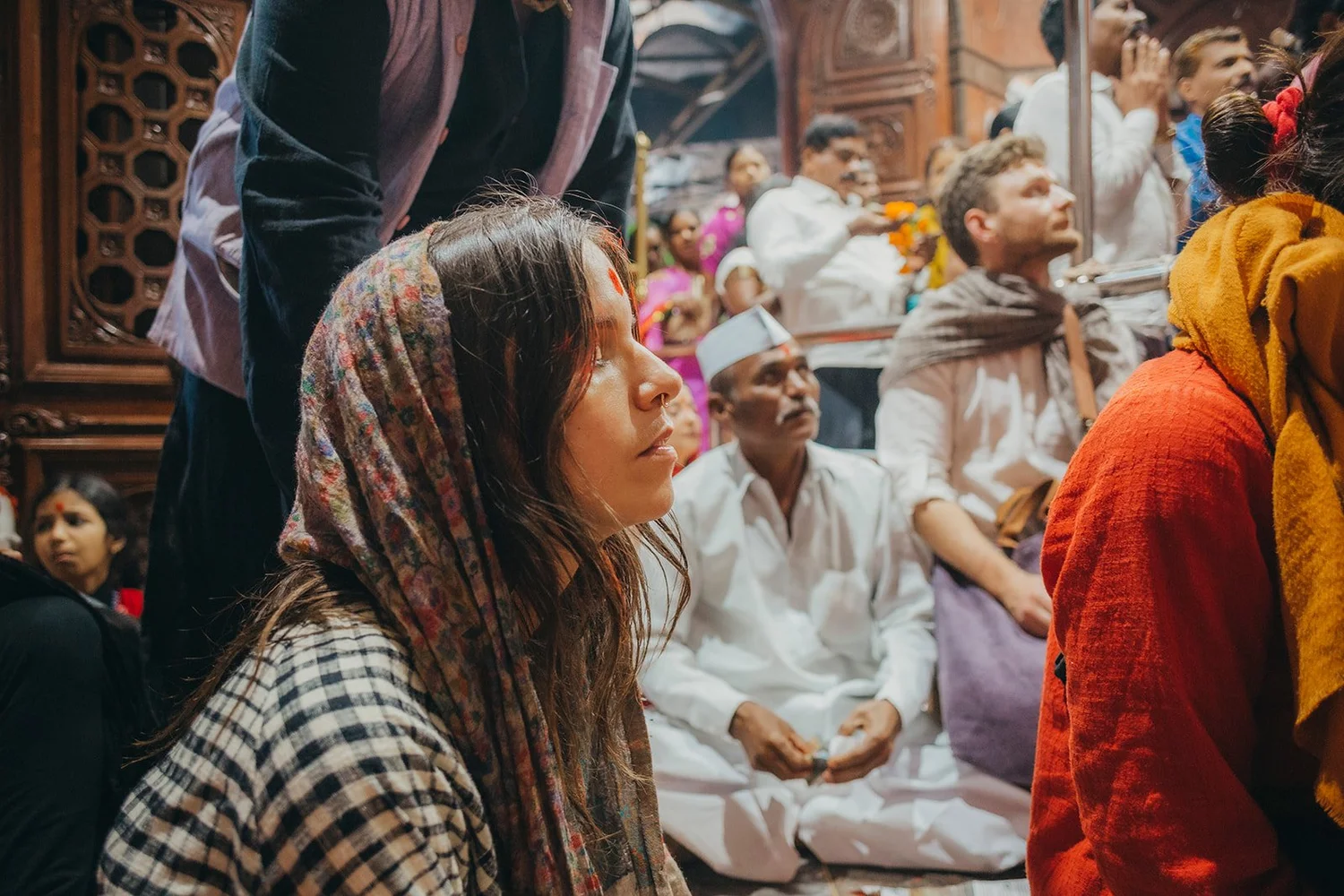 A pilgrim in a headscarf among devotees inside a crowded temple