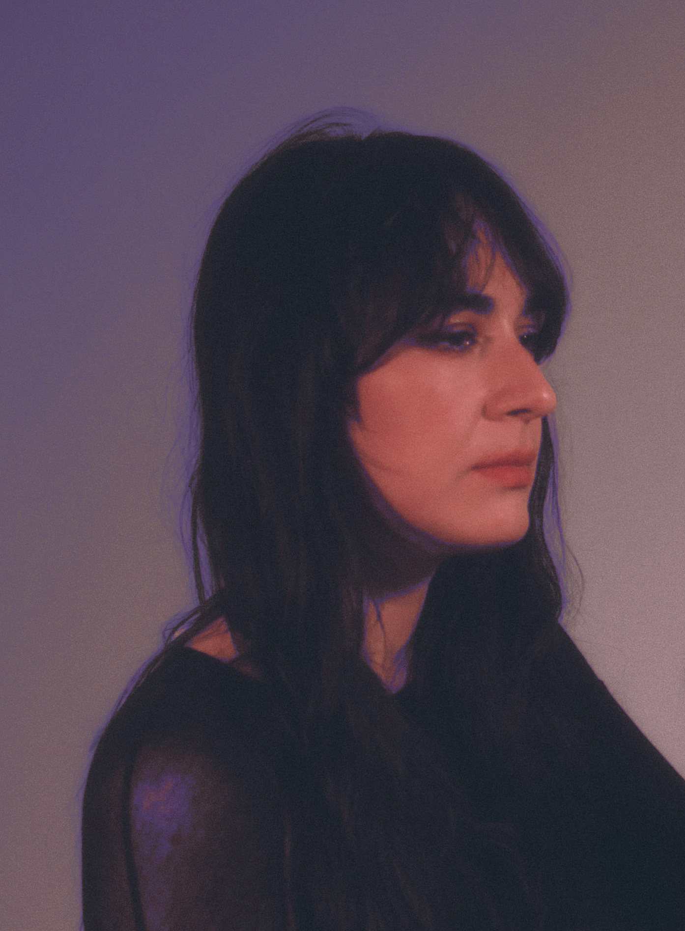 A woman with dark hair and bangs, wearing a black top, is captured in profile against a red patterned background.