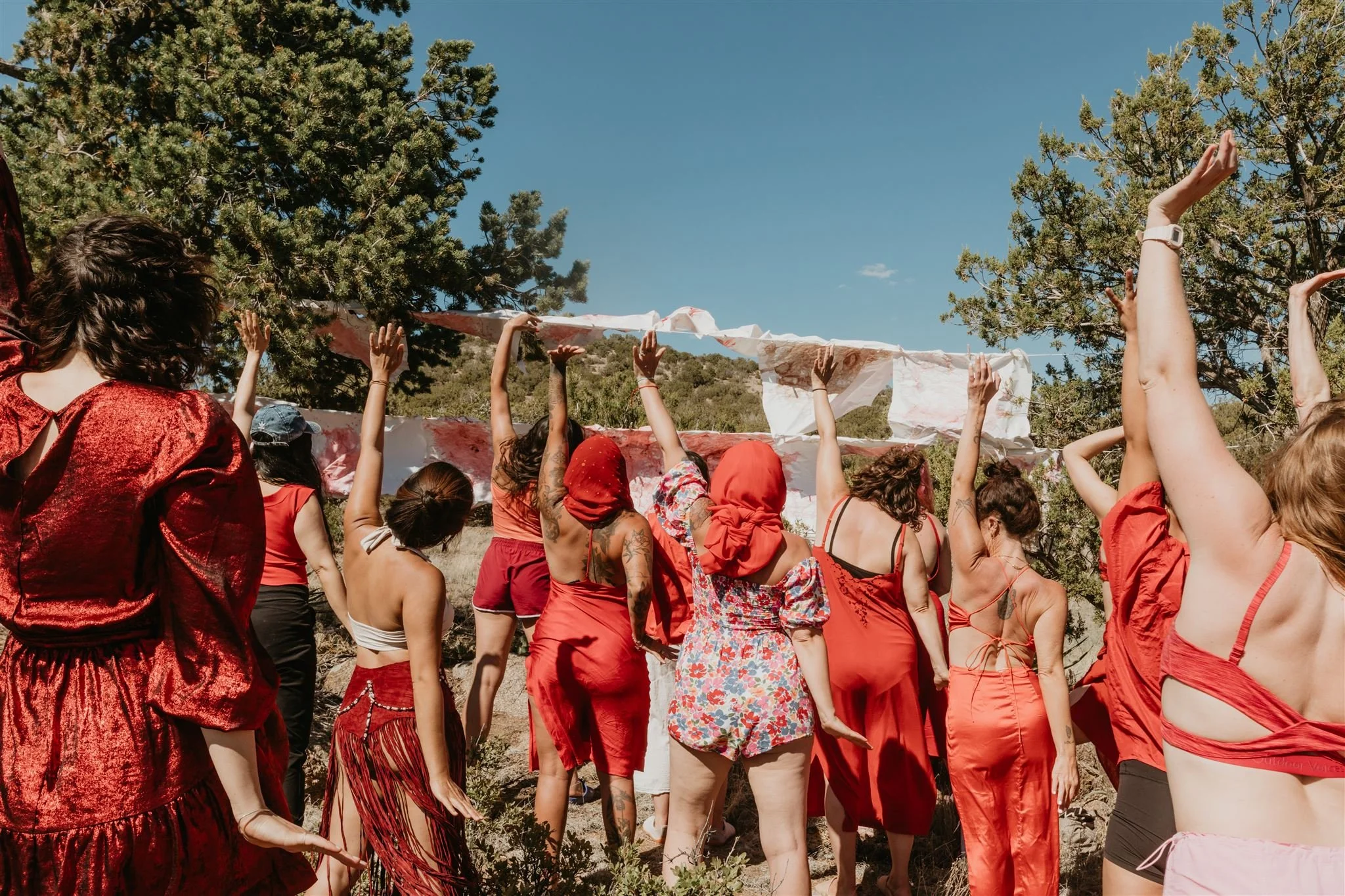Group of women in red clothing participating in a blanket-making activity outdoors on a sunny day.