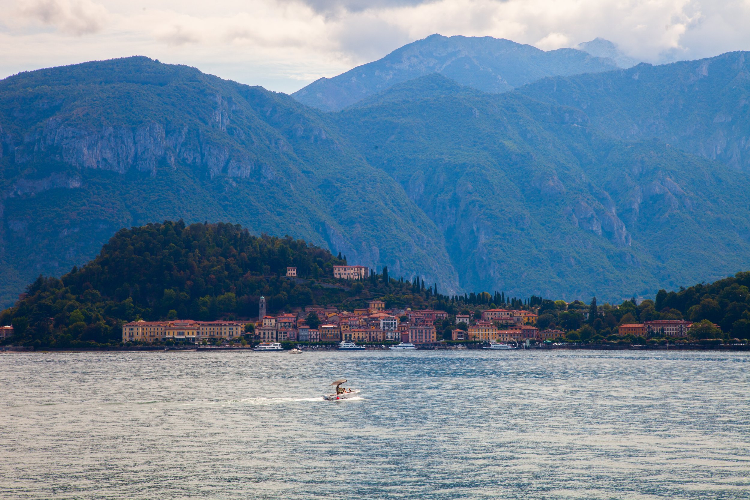 A scenic view of a lakeside town with colorful buildings at the foot of lush green mountains and a boat sailing on the lake.