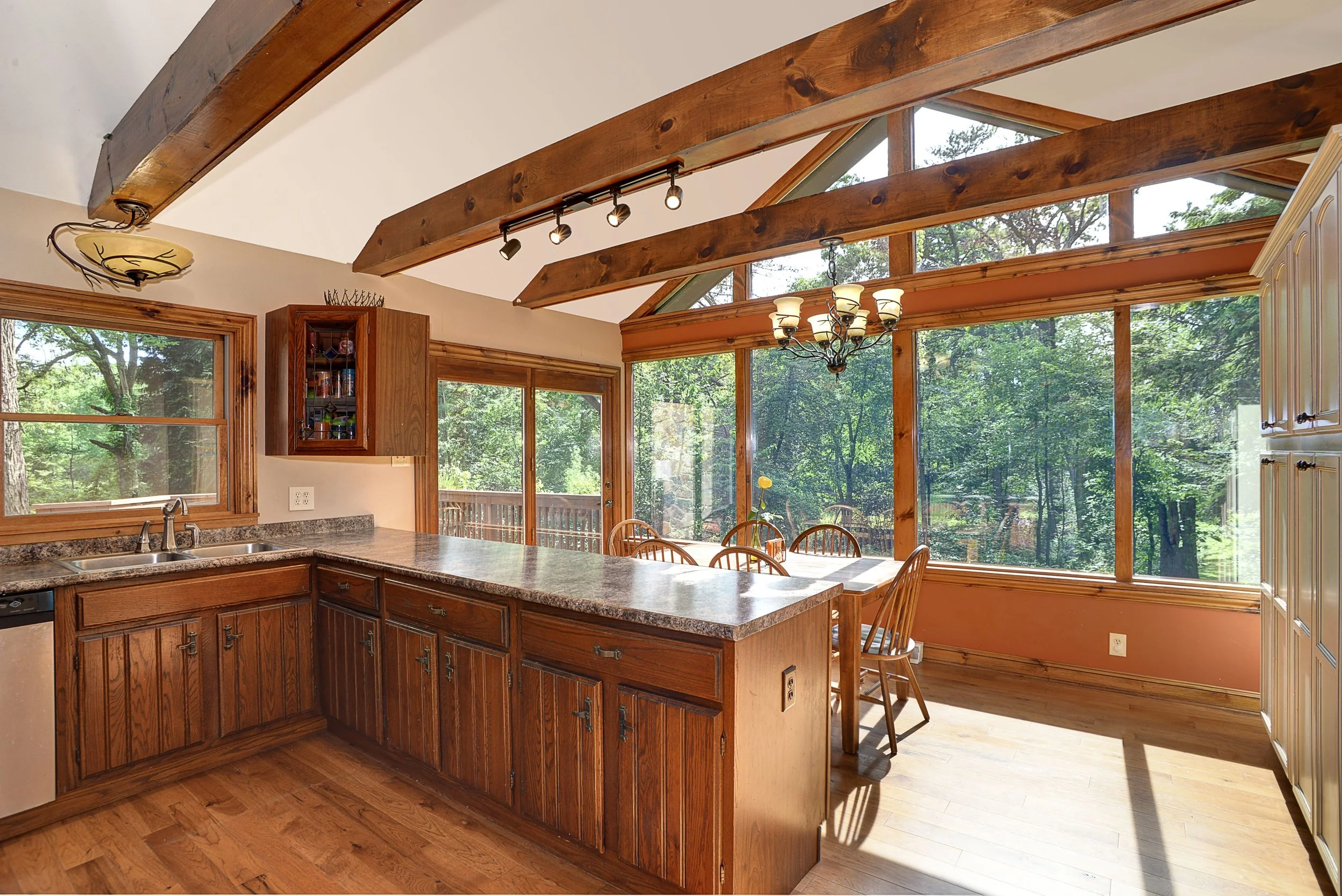 Kitchen with wooden cabinets, granite countertops, large windows, and a dining area with a view of trees outside.