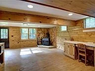Empty rustic living room with wooden walls, large windows, and a stone fireplace