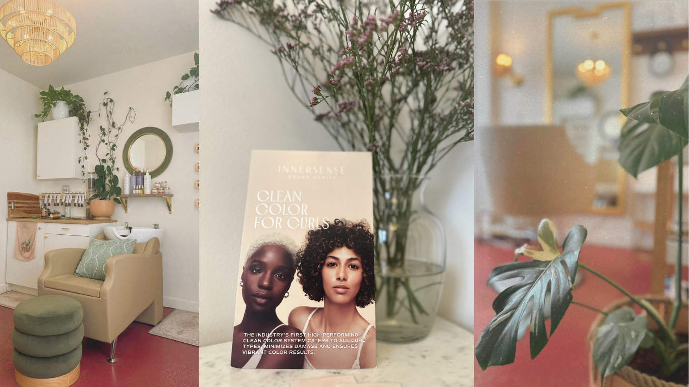 Interior of a beauty salon with a beige armchair, green top, and matching ottoman. Wall decor includes a round mirror, white cabinets, and plants. Center features a brochure titled 'Clean Color for Curls' with images of two women, and a bouquet of pink flowers in a vase. The background shows a mirror, lighting, and shelves.