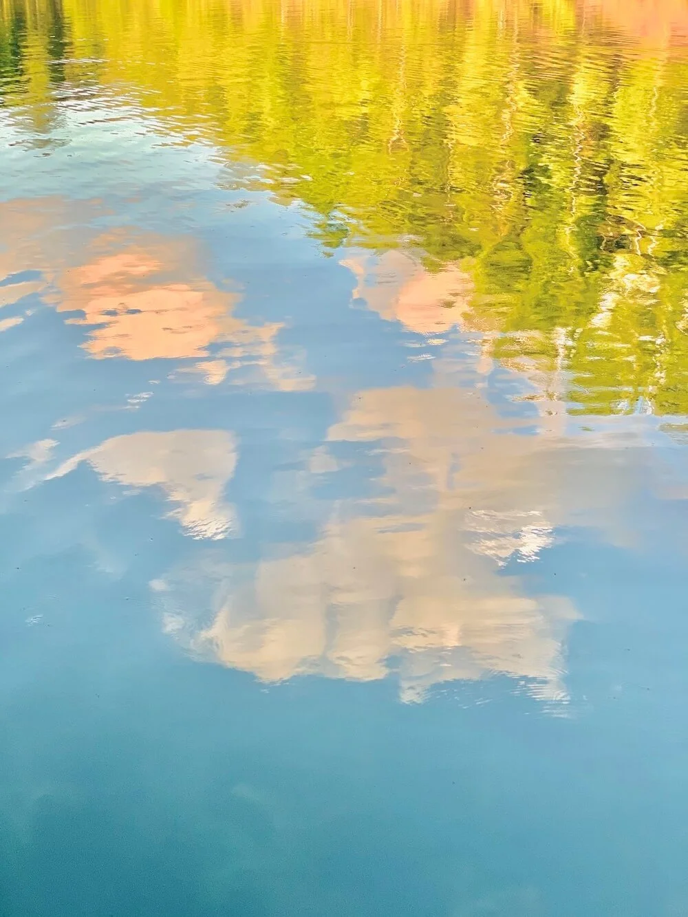 Reflection of trees and clouds on a body of water during sunset.