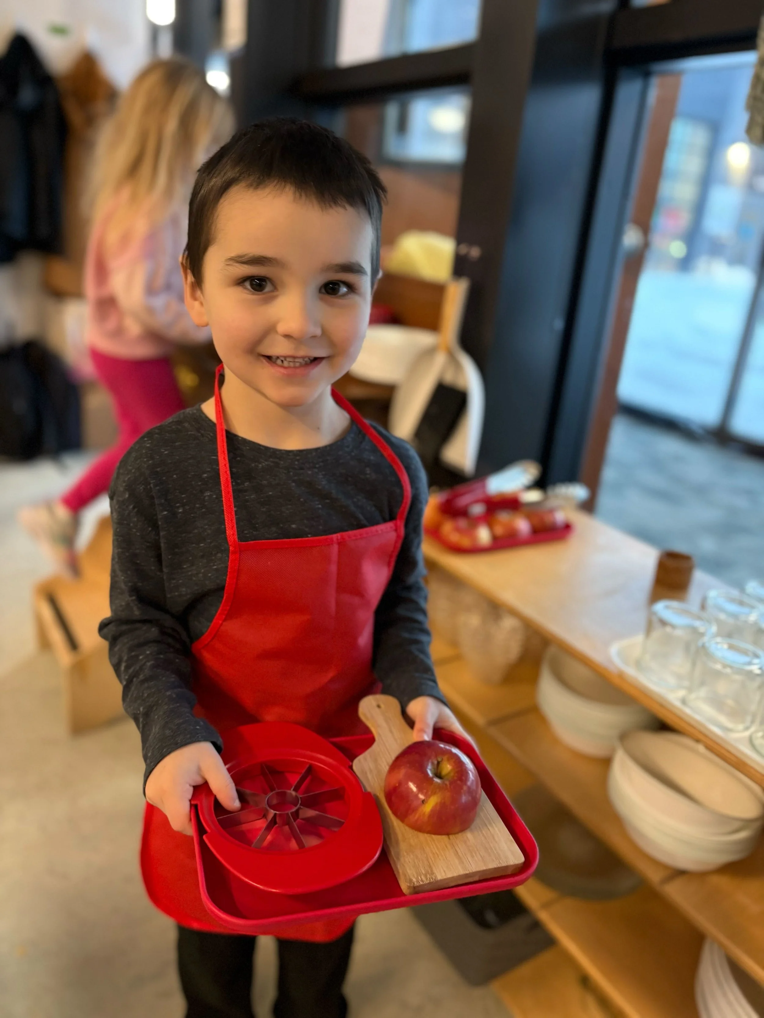 Smiling boy holding red tray, with red apple, and red apple cutter.