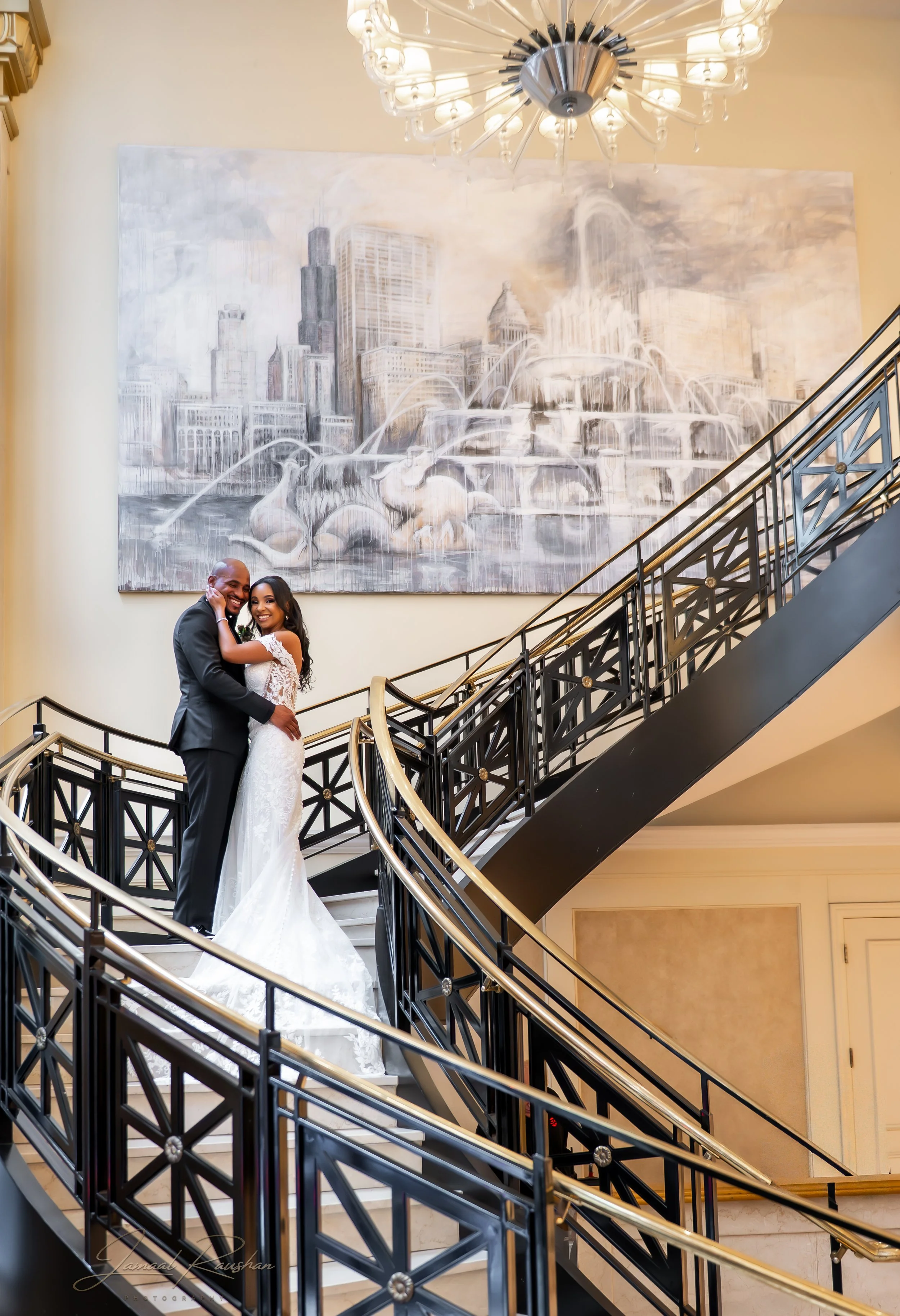 A newlywed couple hugging on a staircase inside the JW Marriott in Chicago, with a large artistic cityscape painting in the background.