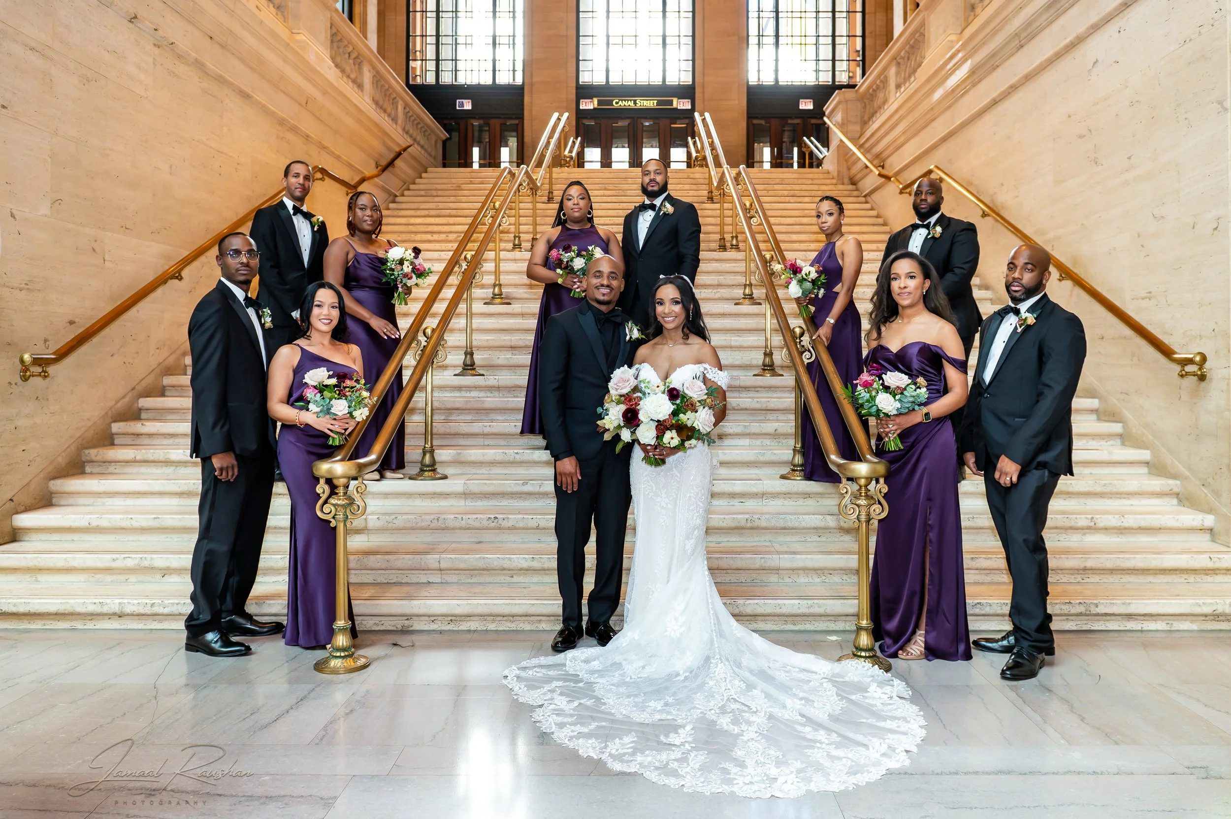 A group of ten people, including a bride and groom, standing on a grand staircase inside Union Station in Chicago. The bride is wearing a white wedding dress and holding a bouquet, and the groom is dressed in a black tuxedo.  