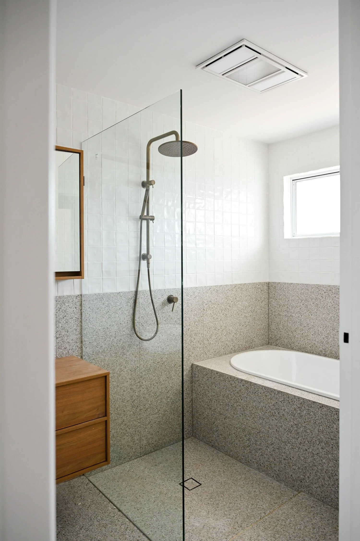 Modern bathroom with walk-in shower, rain shower head, bathtub, wooden storage cabinet, white tiled walls, small window, and ceiling vent.