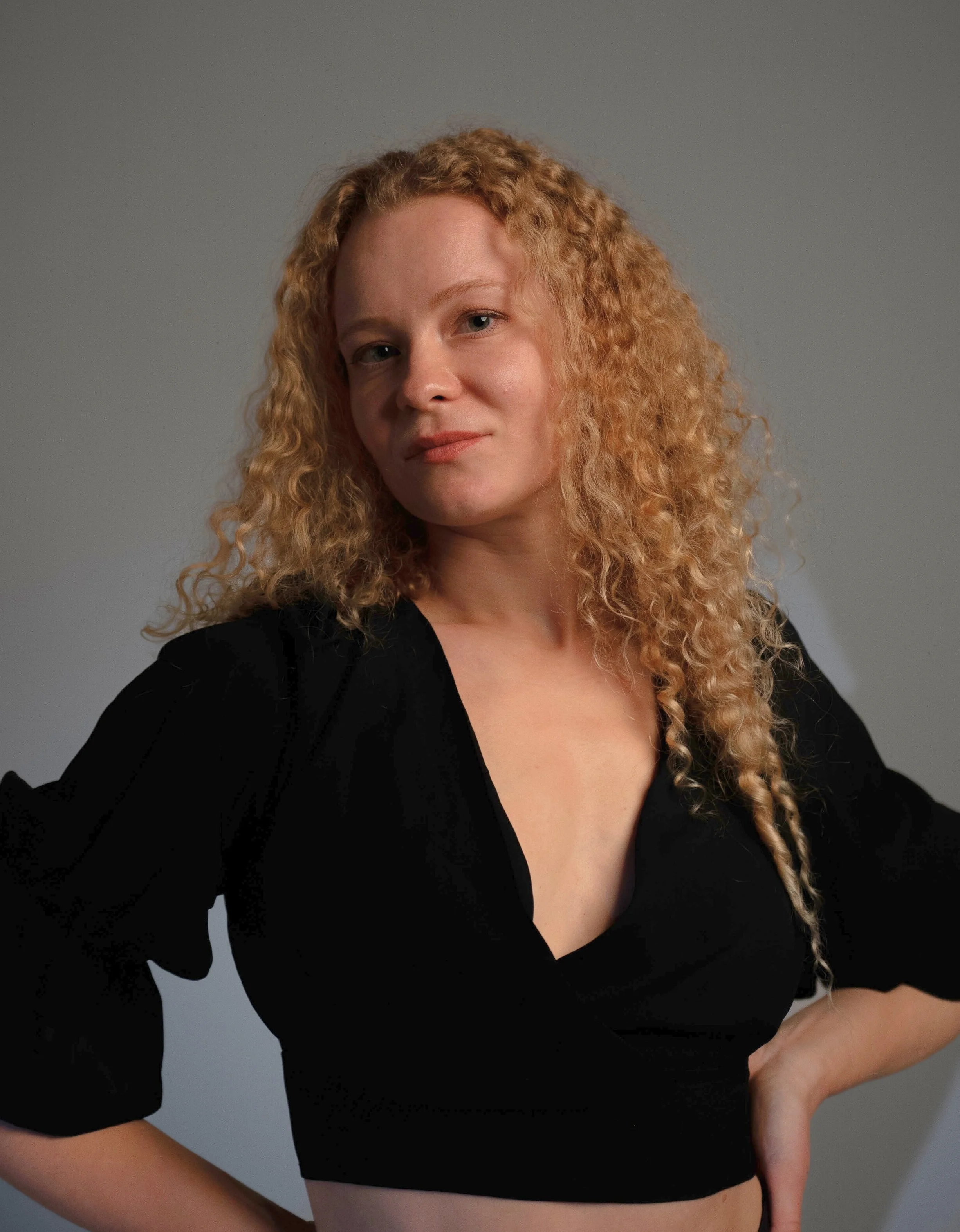 Portrait of a woman with curly blonde hair wearing a black top against a gray background.